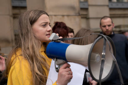 female school striker wearing yellow coat and holding a megaphone